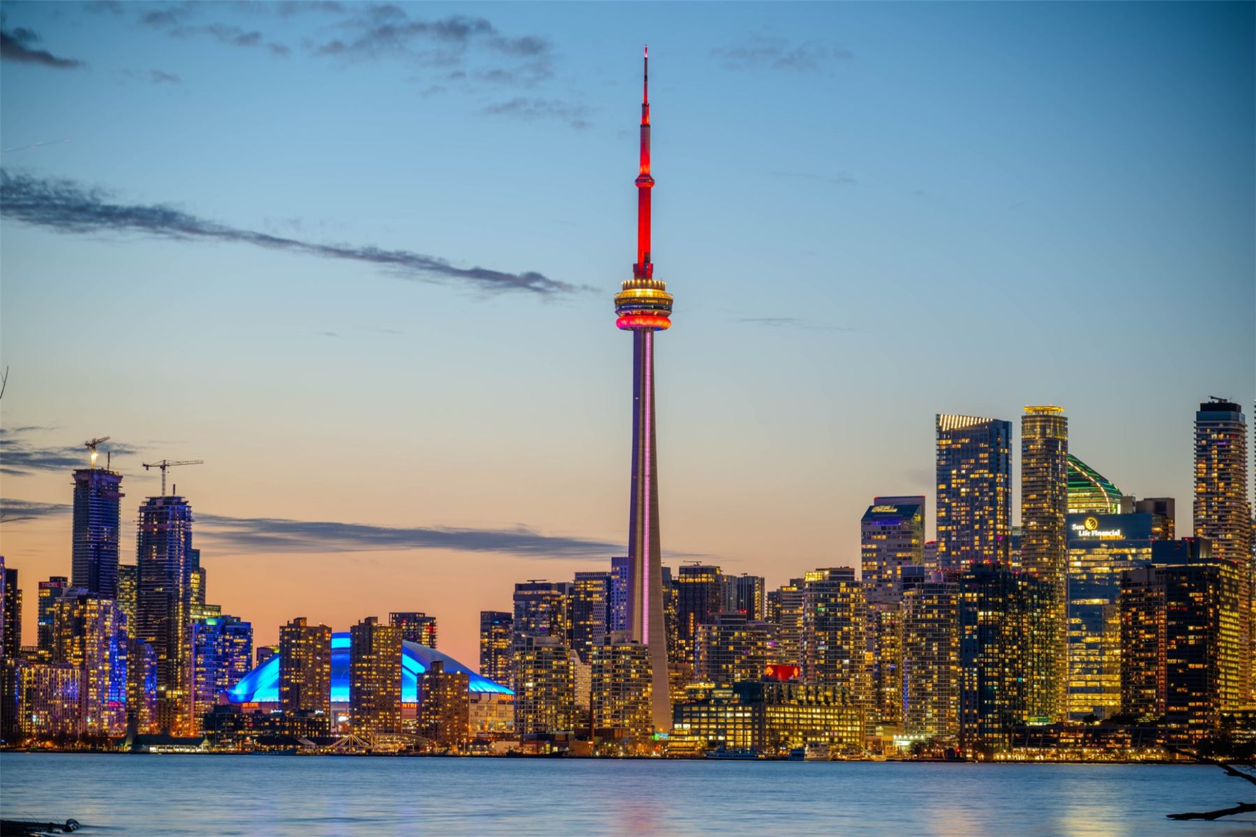 The Toronto skyline and CN Tower lit up at dusk across Lake Ontario