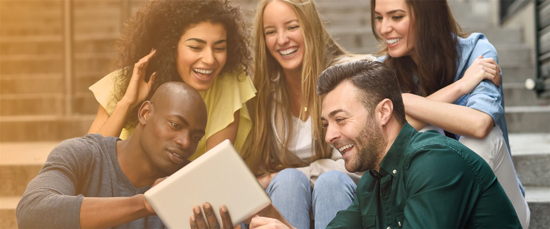 A group of international students laughing together while looking at a tablet