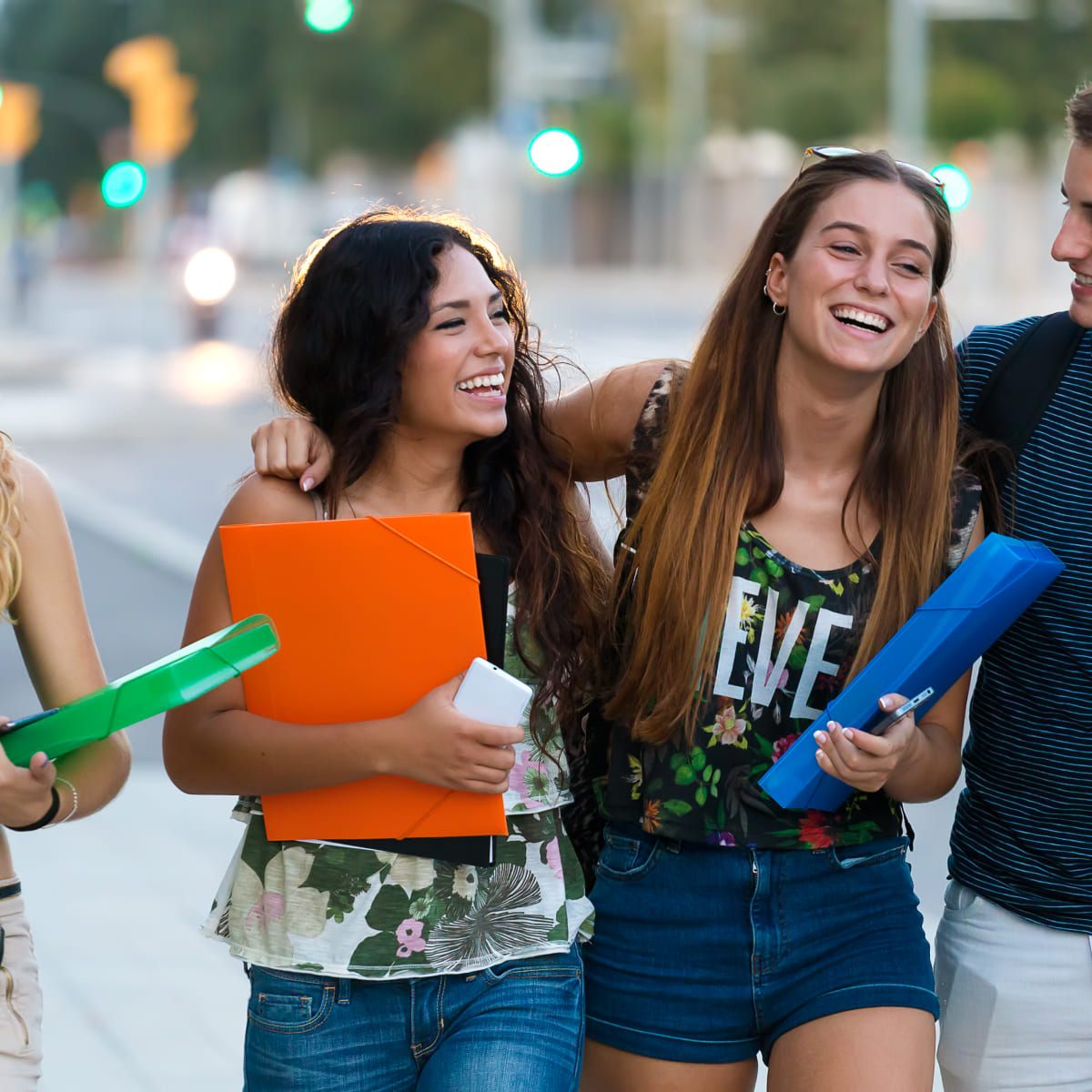 Two students walking down a city street carrying folders and smiling